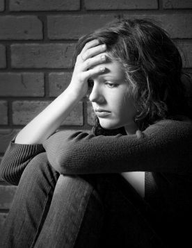 Teenage girl siiting against brick wall in a depressed state